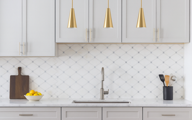 Modern kitchen with Bianco Dolomite Octave mosaic tile backsplash, light gray Shaker cabinets, brass pendant lights, and marble countertop