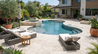 A bright and inviting backyard swimming pool and spa area featuring ivory travertine stone tile decking and coping, styled with simple lounge chairs and greenery in a realistic, sunny home setting.