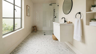 A bright bathroom featuring a white marble penny tile floor with subtle gray veining, styled with a modern white vanity and matte black fixtures in soft natural light to showcase a clean and attainable interior design.