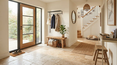 An inviting, realistic home entryway with natural stone floor tiles, styled with a wooden bench and a potted plant in warm natural light.