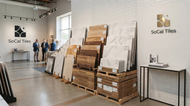 A professional and bright natural stone tile showroom featuring an organized display of premium travertine and marble, with the SoCal Tiles logo and name featured in solid black on the far left wall.