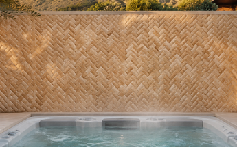 Antico Onyx Travertine round-faced herringbone mosaic installed on an outdoor accent wall behind a backyard hot tub.