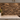 A kitchen backsplash made of horizontal dark brown and black marble tiles with warm gold veining, installed above a light beige marble countertop with gray cabinets.